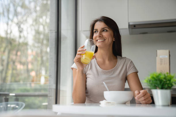 Happy woman having breakfast at home Happy Latin American woman relaxing at home and having breakfast in the morning - lifestyle juice drink stock pictures, royalty-free photos & images