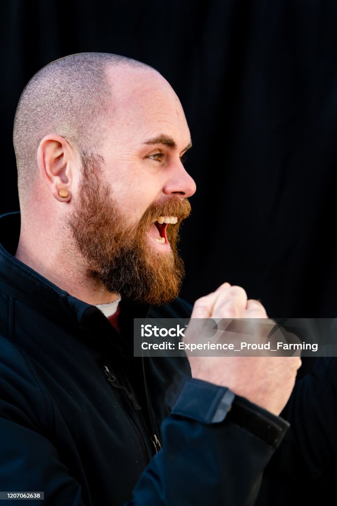 Hipster Young man with full beard and earplug cheers with clenched fists in front of a black background. Adults Only Stock Photo