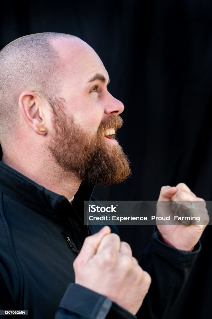 Hipster Young man with full beard and earplug cheers with clenched fists in front of a black background. Adults Only Stock Photo