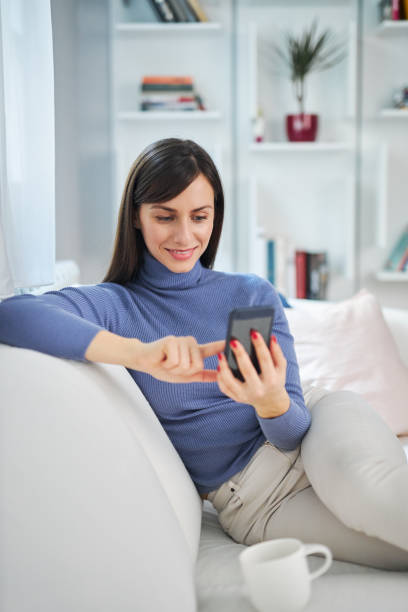 istock Young charming brunette sitting on couch in her beautiful home and typing message. 1207062915