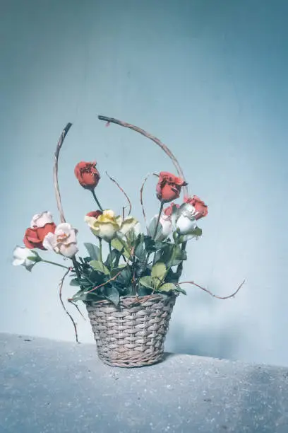 an old flower basket with roses in front of a wall