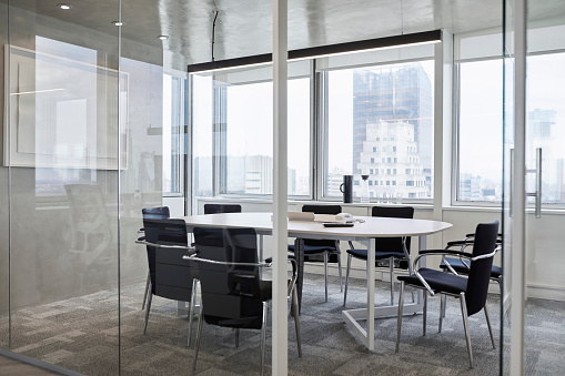 Empty chairs around table in board room. Modern meeting room against window in office. Furniture seen through glass walls in conference room.