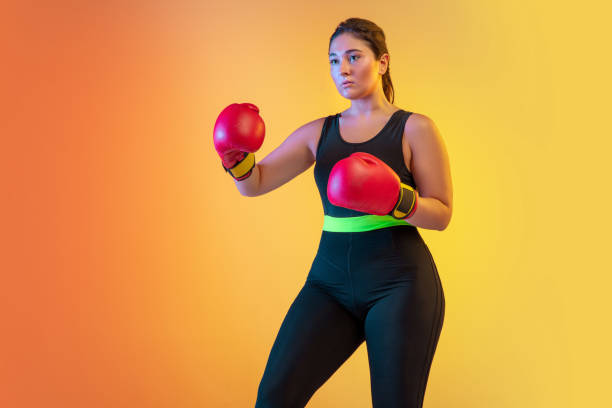 istock Young caucasian plus size female model's training on gradient orange background 1207070817
