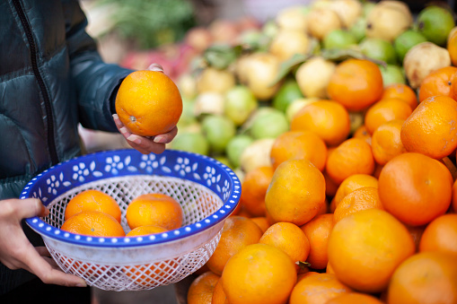 Close-up of Woman's hand choosing fresh oranges and collecting in basket for buying at market.