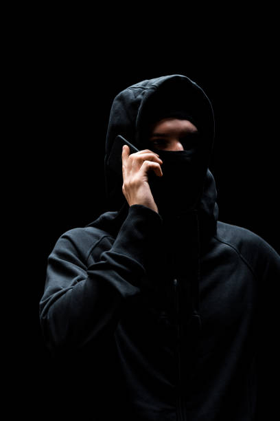 istock hacker in hood and mask talking on smartphone isolated on black 1207075658