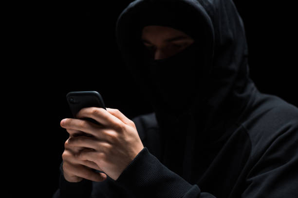 istock selective focus of hacker in mask using smartphone isolated on black 1207075742