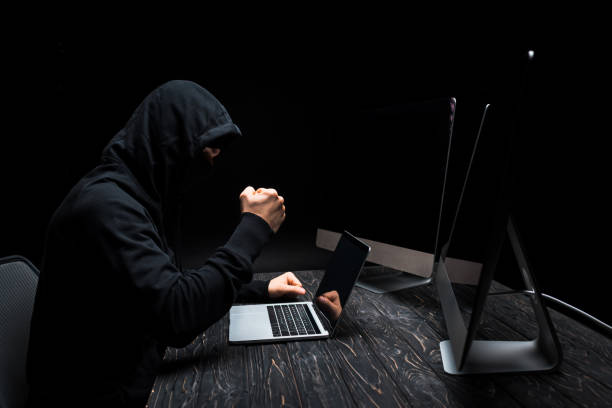 istock angry hacker with clenched fist near laptop and computer monitors with blank screen isolated on black 1207075767