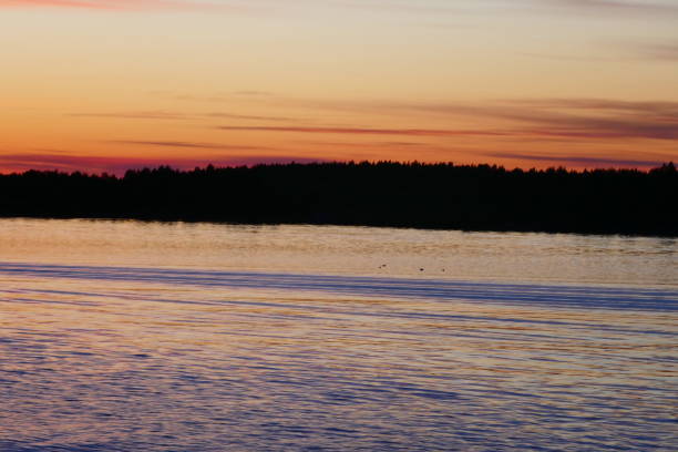 istock Find & Replace Sunset and blue skies over the forest which is in silhouette on the water's edge on Lake Ladoga. Water reflecting the light 1207076034