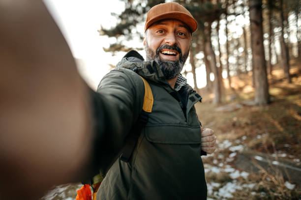 istock Happy mature backpacker holding camera and taking a selfie on a mountain during winter day 1207082910