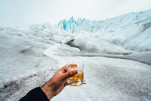 Pov view of a man drinking whisky on Perito Moreno glacier. He's holding a glass of whisky.
