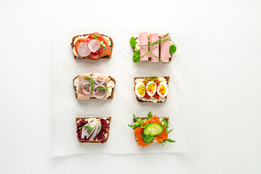 Selection of Danish smorrebrod open sandwiches on parchment paper on white background. Top view with copy space, horizontal orientation