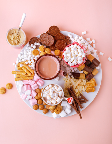 Hot chocolate, marshmallows, chocolates and cookies charcuterie board on pink background. Top view, portrait orientation