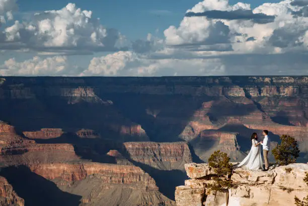 Photo of A couple stands far on the edge of a cliff with a spectacular view of the canyon, a stunning sky with clouds