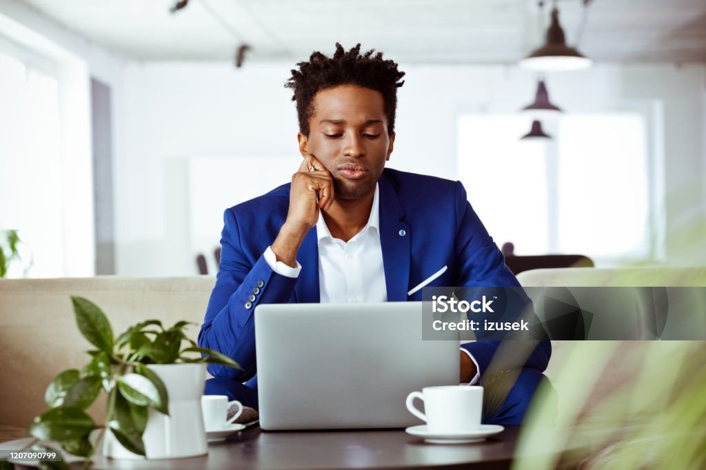 Bored male financial advisor looking at laptop Bored male financial advisor looking at laptop. Mid adult executive is sitting in office. He is working. Boredom Stock Photo