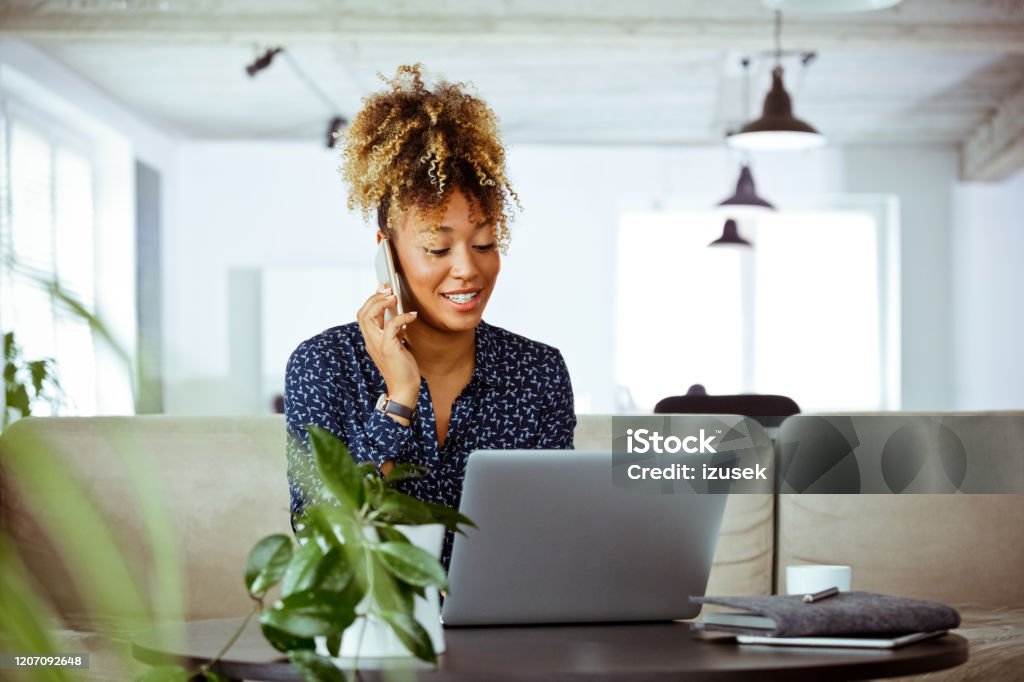 Businesswoman dealing with client through phone Smiling business worker dealing with client through smart phone. Mid adult female expert is working in office. She is related to financial occupation. Financial Advisor Stock Photo