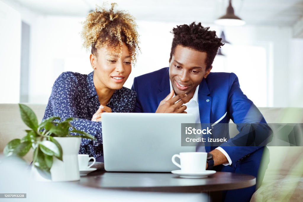 Financial advisors smiling while using laptop Financial advisors smiling while using laptop. Corporate workers are planning finance. They are working in office. African-American Ethnicity Stock Photo