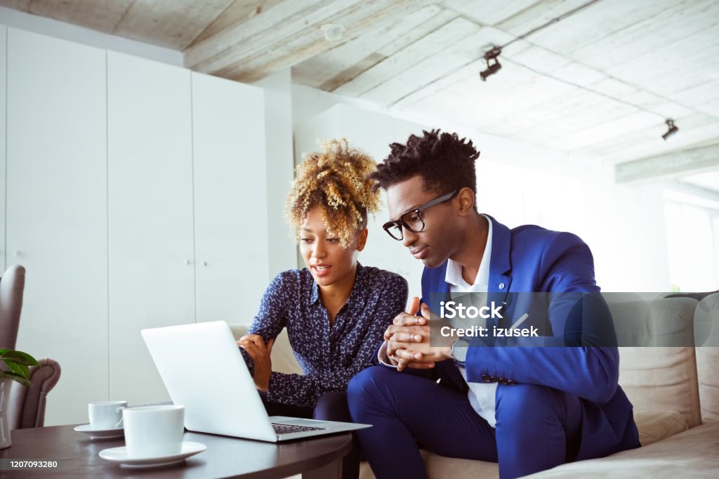 Financial experts discussing over laptop in office Financial experts discussing over laptop in office. Entrepreneurs are planning business. They are sitting on sofa. 30-34 Years Stock Photo