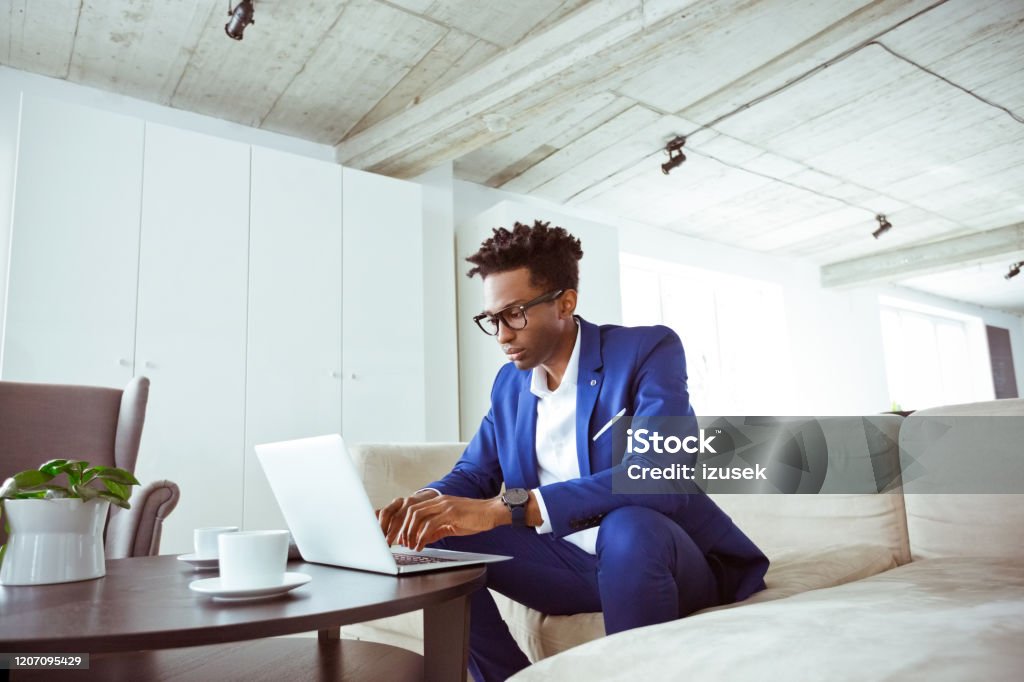 Serious financial expert using laptop in office Well-dressed financial expert using laptop at work place. Serious businessman is working while sitting on sofa. He is concentrated towards his work. Financial Advisor Stock Photo
