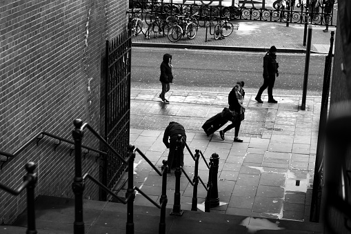 January 28, 2020 - London, UK: four passers-by passing tunnel steps with bannister and iron gate - a street life view in London, b&w