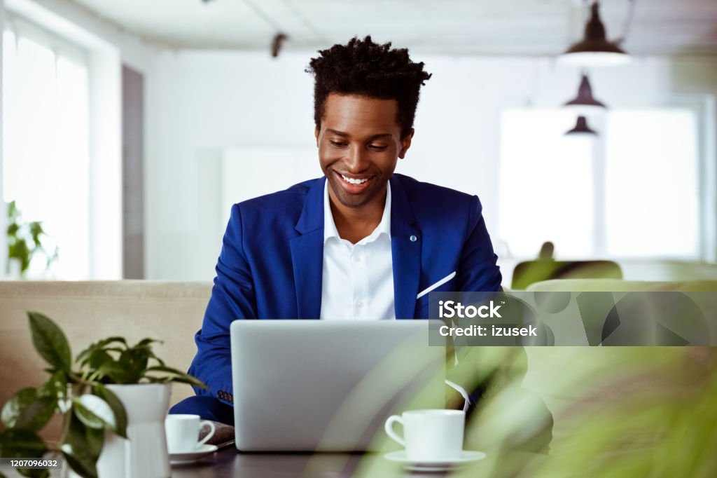 Smiling entrepreneur working on investment plans Smiling entrepreneur working on investment plans. Mid adult male corporate expert is using laptop. He is with confident look on his face. Suit Stock Photo