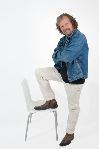 mature man in white pants and blue denim jacket put down his foot on the white chair