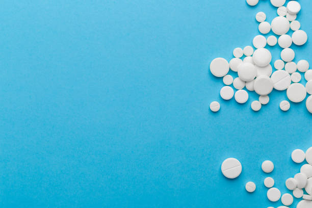 istock scattered white pills on a blue table. Layout for special offers such as advertising or other ideas. The concept of medicine, pharmacy and healthcare. Space for copy. 1207097405