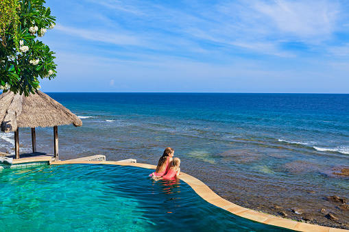 Happy child have fun on summer beach holiday. Young mother, kid relax at edge of infinity swimming pool. Beautiful sea view from hill top. Cruise family lifestyle, summer travel on tropical holiday.