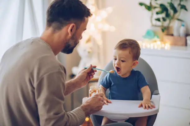 Father feeding baby boy in high chair