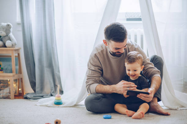 Watching cartoons together Father and son sitting on floor and watching favorite cartoon on mobile phone child care photos stock pictures, royalty-free photos & images