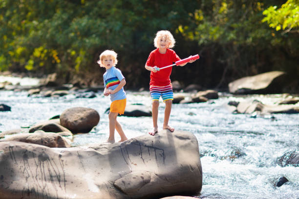 Children hiking in Alps mountains crossing river. Kids play in water at mountain in Austria. Spring family vacation. Little boy and girl on hike trail. Outdoor fun. Active recreation with children.