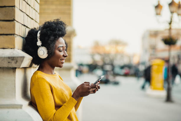 Young woman listening music Photo of African American modern woman on the street listening music with headphones arts and entertainment stock pictures, royalty-free photos & images