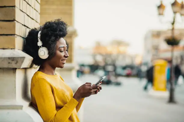 Photo of African American modern woman on the street listening music with headphones