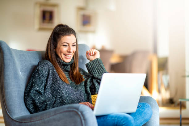 Happ young woman using notebook while working from home Shot of smiling woman sitting in the armchair and using laptop while working from home. Home office. happ stock pictures, royalty-free photos & images