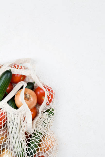 istock White mesh shopping bag with red tomatoes, bow and green cucumbers on white background. 1207106087