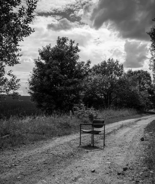 an old broken chair on a dirt road in summer in black and white