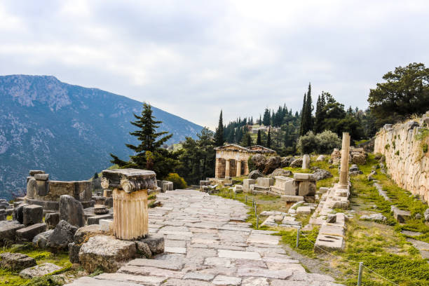istock Rock walkway down hill in ancient Delphi Greece past ionic columns and parts of temples and past a reconstructed treasury with mountain in distance 1207111696
