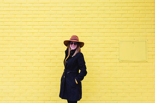 young woman outdoors using mobile phone and smiling. Lifestyle in the city. yellow brick wall background