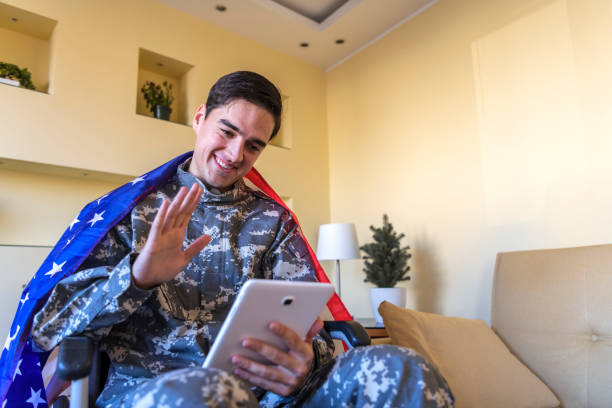 istock Happy Young War Veteran is Communicating over the Digital Tablet and Holding a US Flag 1207112649