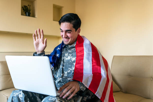 istock Retired Soldier With Physical Disabilities is Using a Laptop and Holding US Flag 1207112679