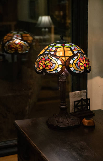 Ingeniører Ledig på Ornate Table Lamp With Stained Glass Lampshade Closeup On Dark Background  Glowing Mosaic Lamp Reflected In Blurred Glass Window Vintage Lamp Shade  Made Of Colorful Glass Pieces Stock Photo - Download Image