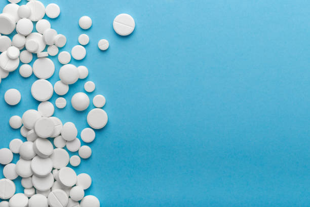 istock scattered white pills on a blue table. Layout for special offers such as advertising or other ideas. The concept of medicine, pharmacy and healthcare. Space for copy. 1207115528