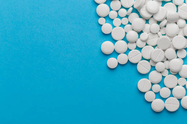 istock scattered white pills on a blue table. Layout for special offers such as advertising or other ideas. The concept of medicine, pharmacy and healthcare. Space for copy. 1207115546