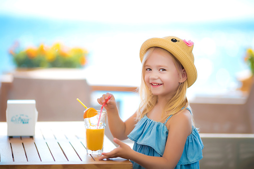 Beautiful blonde girl sitting at the table in the cafe outdoors drinking juice and eating desserts.