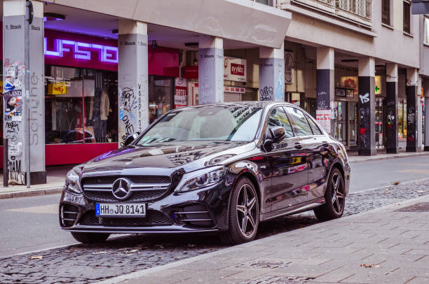 Berlin, Germany – November 20, 2025: A black sedan drives along a wet empty city street lined with trees and fallen leaves.