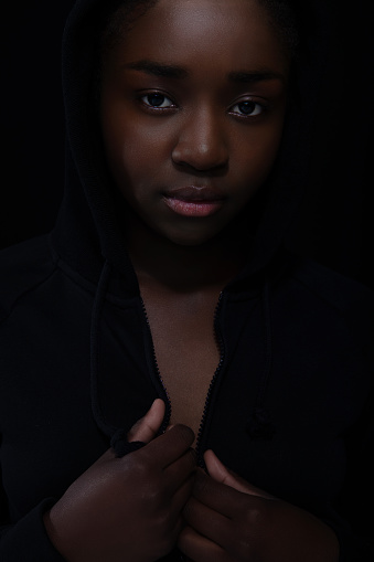 Cool and reticent woman with dark skin and attitude wearing hoodie. High quality low-key studio portrait.