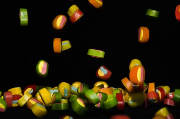 Many sweet and colourful candies are falling down to the table with black background