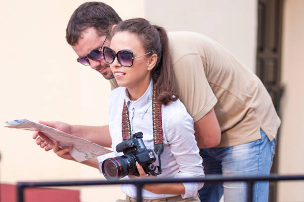istock Smiling Caucasian Couple Travelling with Trolley Suitcase Outdoors. Checking Route Using City Map. Posing with Photocamera.Horizontal Image 1207127936
