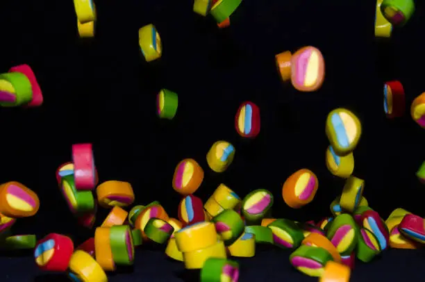Many sweet and colourful candies are falling down to the table with black background