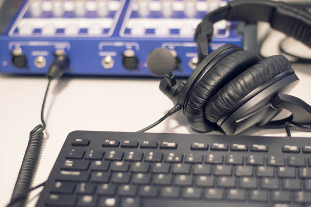 istock Studio time. Close-up headphones  with other professional audio studio equipments. Microphone for podcasts and studio headphones on a PC keyboard on a black background, horizontal frame stock photo. 1207130414