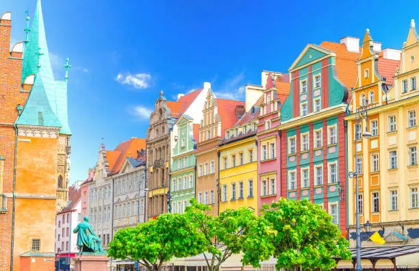 Photo of Row of colorful buildings with multicolored facade and wall of Old Town Hall building on cobblestone Rynek Market Square with green trees in old town historical city centre of Wroclaw, Poland